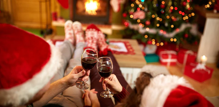 Black Friday: How To Buy Wine For Anyone During The Holidays 1 A couple cheersing Chtistmas with wine by a tree and fireplace. TAG Liquor Stores Canada | Beer, Wine, Spirits & Gift Baskets Canada-wide Delivery
